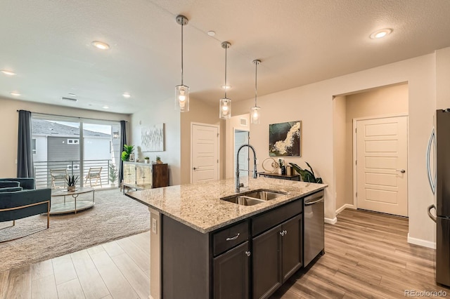 kitchen with light wood-style flooring, light stone counters, a sink, open floor plan, and appliances with stainless steel finishes