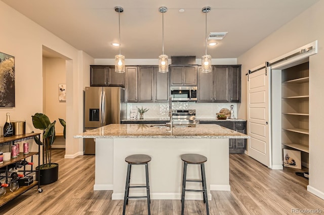 kitchen featuring an island with sink, light wood-style floors, stainless steel appliances, and visible vents