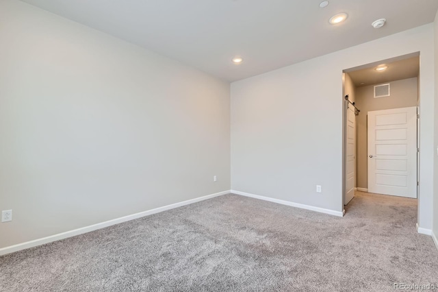 carpeted spare room with baseboards, recessed lighting, a barn door, and visible vents