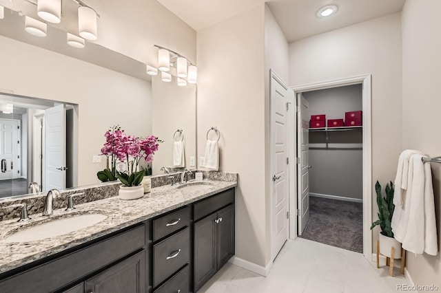 full bathroom with baseboards, a spacious closet, double vanity, and a sink