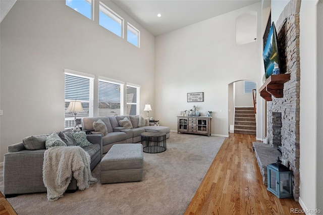 living room with a stone fireplace, light hardwood / wood-style floors, and a high ceiling