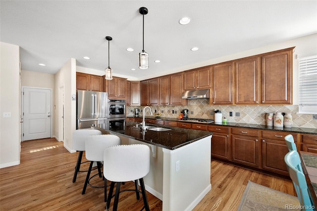 kitchen with sink, hanging light fixtures, a center island with sink, appliances with stainless steel finishes, and decorative backsplash