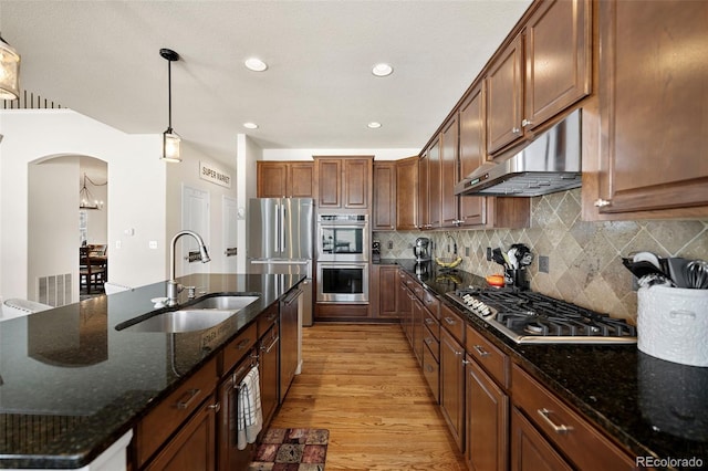 kitchen with sink, dark stone countertops, hanging light fixtures, light hardwood / wood-style floors, and stainless steel appliances