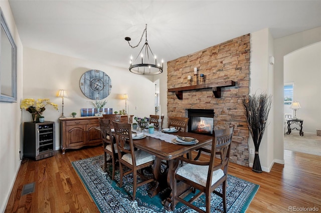 dining space with an inviting chandelier, hardwood / wood-style flooring, a fireplace, and beverage cooler