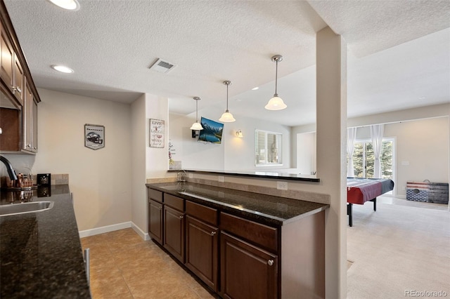 kitchen featuring sink, dark brown cabinetry, a textured ceiling, decorative light fixtures, and dark stone counters