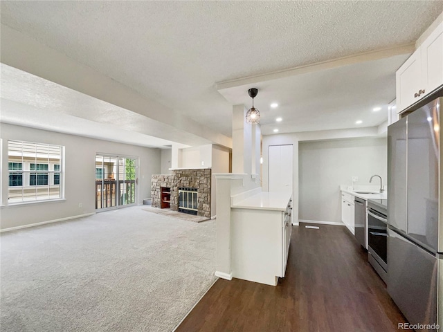 kitchen with a stone fireplace, dark hardwood / wood-style floors, a textured ceiling, appliances with stainless steel finishes, and white cabinetry