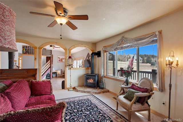 carpeted living room featuring ceiling fan, a wood stove, and a textured ceiling