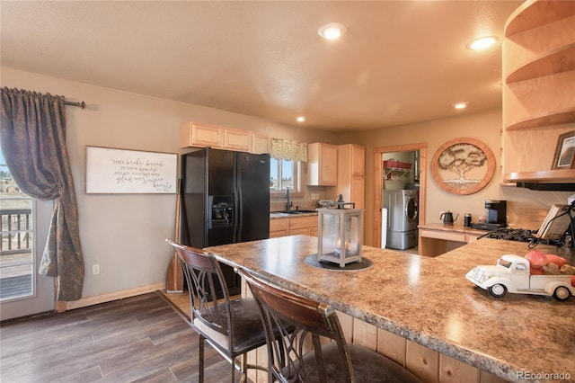 kitchen featuring a kitchen breakfast bar, dark hardwood / wood-style flooring, black fridge, sink, and separate washer and dryer