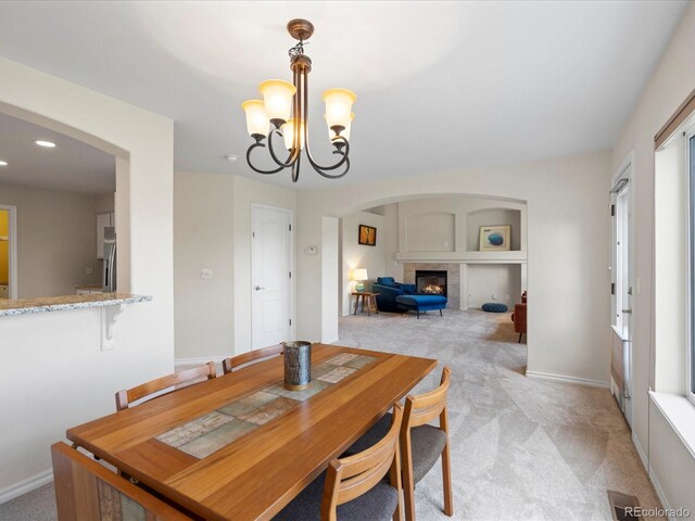 7400 W Grant Ranch Blvd Unit 19, Littleton, CO 80123 - dining room featuring arched walkways, light carpet, a glass covered fireplace, a chandelier, and baseboards