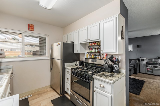 kitchen with white cabinets, stainless steel appliances, light wood-type flooring, and a textured ceiling