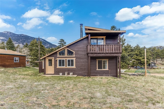 rear view of house with a mountain view, a balcony, and a yard