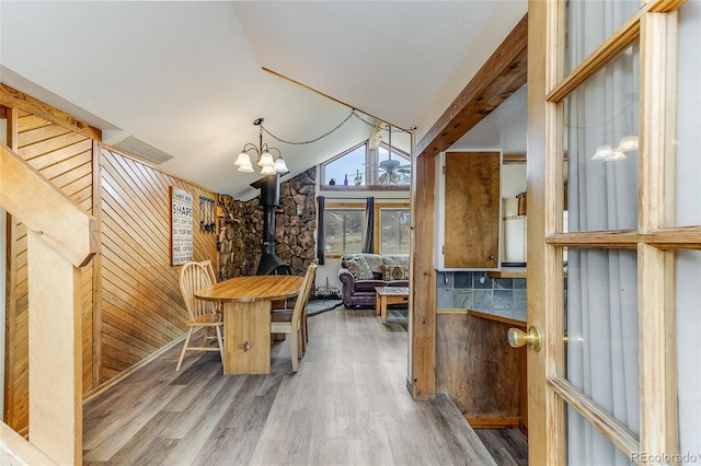 dining space with hardwood / wood-style flooring, wooden walls, a wood stove, lofted ceiling, and a chandelier