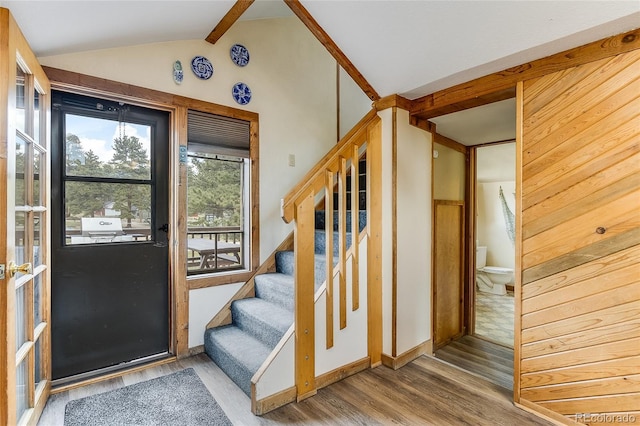 foyer entrance with hardwood / wood-style flooring, wood walls, and vaulted ceiling with beams