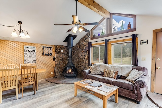 living room featuring ceiling fan with notable chandelier, beamed ceiling, a wood stove, wood walls, and light hardwood / wood-style flooring