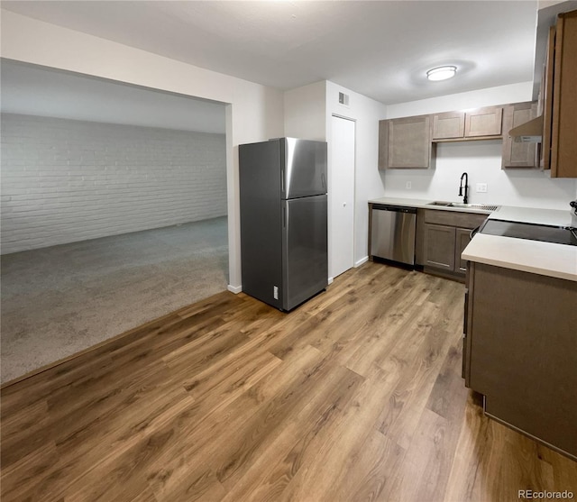 kitchen with hardwood / wood-style floors, stainless steel appliances, brick wall, and sink