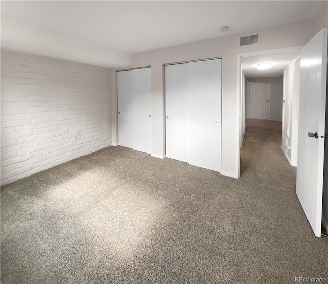 unfurnished bedroom featuring two closets, brick wall, and dark carpet