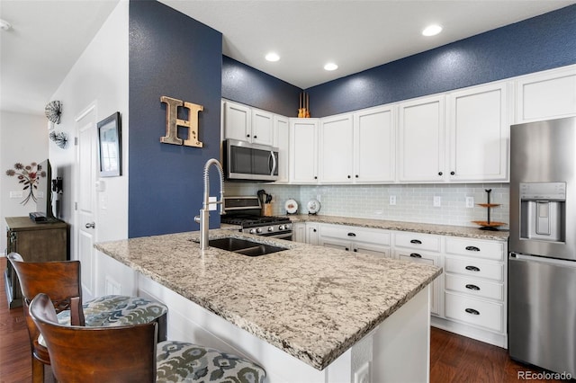 kitchen with appliances with stainless steel finishes, dark wood finished floors, decorative backsplash, a sink, and a textured wall