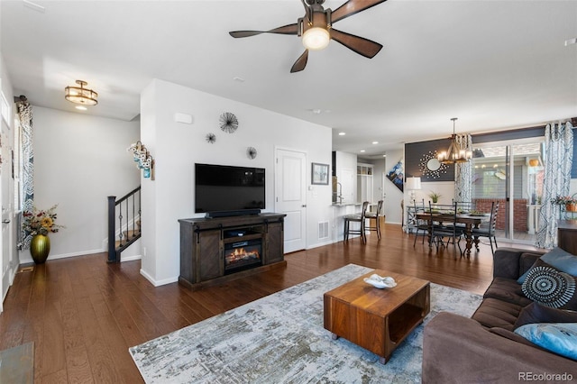 living area featuring stairway, a chandelier, wood finished floors, baseboards, and a glass covered fireplace