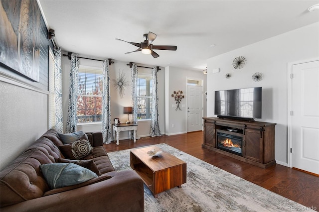 living area featuring ceiling fan, dark wood finished floors, baseboards, and a glass covered fireplace