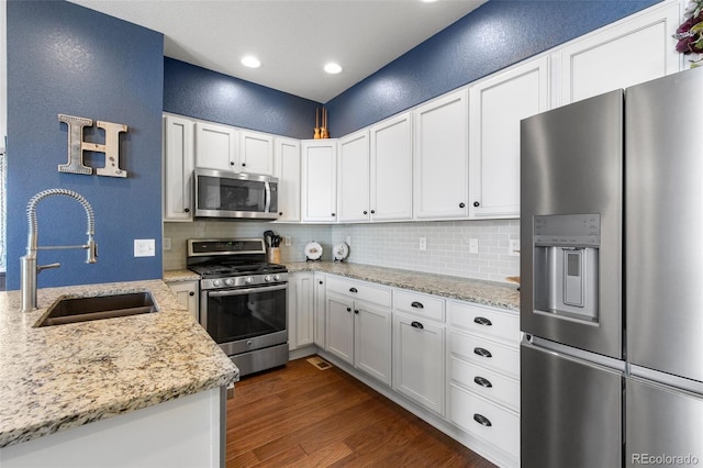 kitchen featuring appliances with stainless steel finishes, a sink, a textured wall, backsplash, and dark wood-style floors
