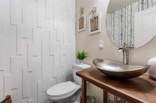 half bath featuring a sink, toilet, and a textured wall