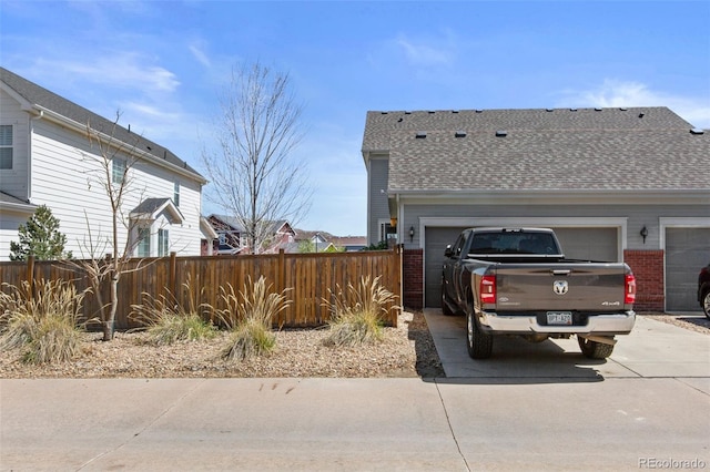 view of home's exterior with concrete driveway, brick siding, fence, and a shingled roof