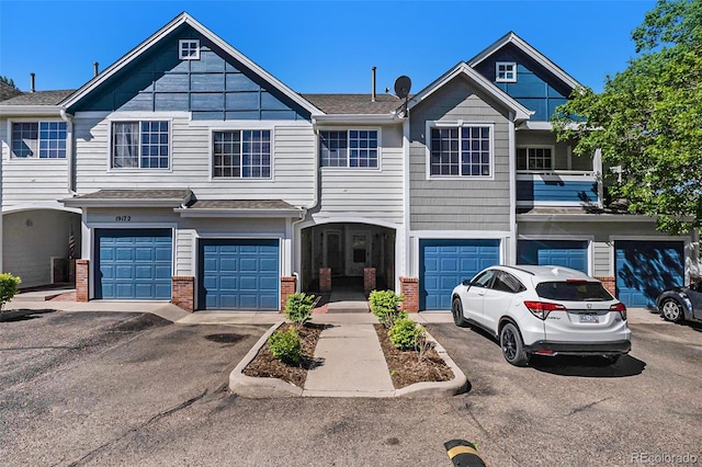 townhome / multi-family property featuring brick siding, an attached garage, and roof with shingles