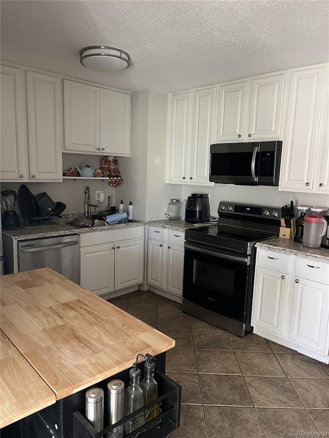 kitchen featuring dark tile patterned floors, stainless steel appliances, light stone counters, white cabinets, and a textured ceiling