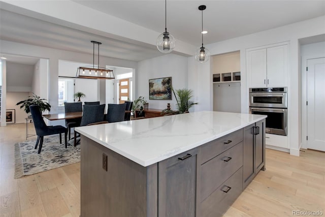 785 Delechant Dr, Erie, CO 80516 - kitchen featuring double oven, light wood finished floors, a kitchen island, light stone counters, and hanging light fixtures