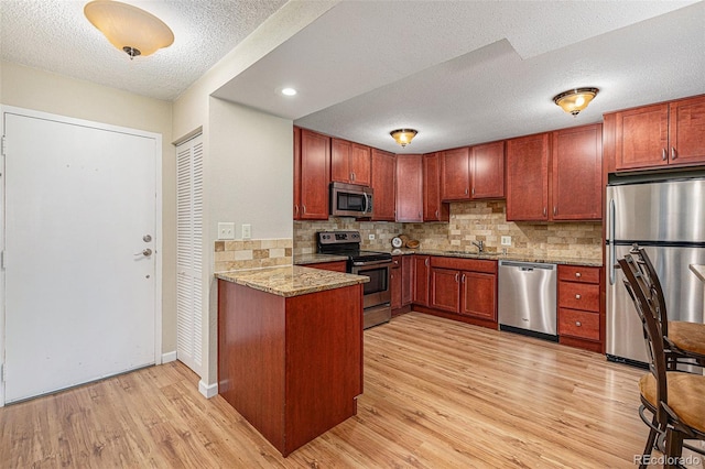 kitchen with light stone countertops, tasteful backsplash, light hardwood / wood-style floors, a textured ceiling, and appliances with stainless steel finishes