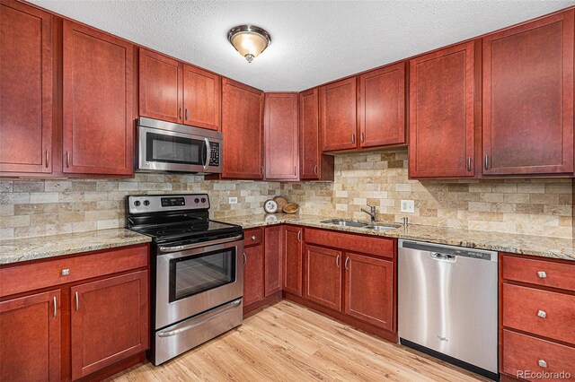 kitchen featuring light stone counters, sink, light hardwood / wood-style flooring, and appliances with stainless steel finishes