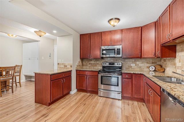 kitchen featuring light stone counters, light wood-type flooring, sink, and appliances with stainless steel finishes