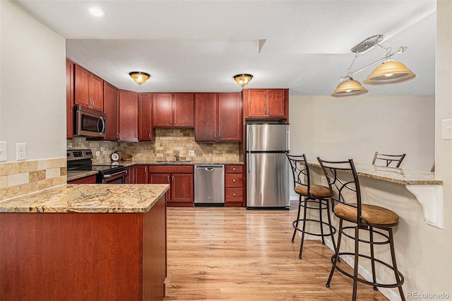 kitchen with sink, hanging light fixtures, stainless steel appliances, kitchen peninsula, and decorative backsplash