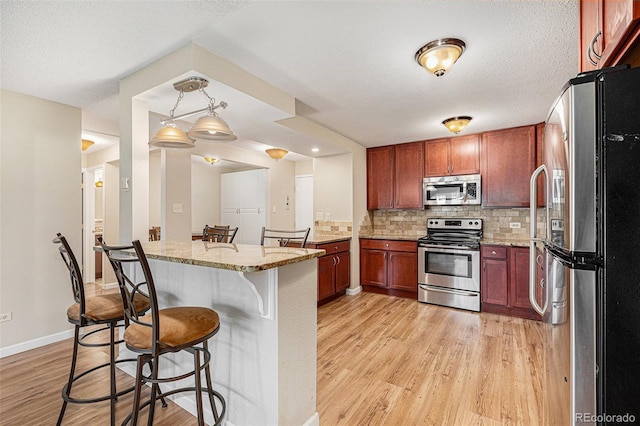 kitchen with light stone countertops, stainless steel appliances, tasteful backsplash, pendant lighting, and a breakfast bar area