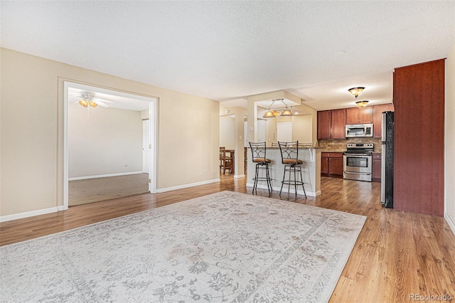 kitchen with ceiling fan, a kitchen breakfast bar, tasteful backsplash, light hardwood / wood-style floors, and appliances with stainless steel finishes