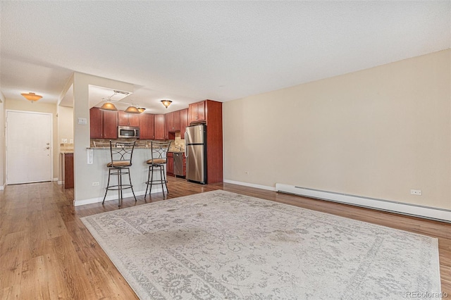 interior space featuring a kitchen bar, decorative backsplash, light wood-type flooring, stainless steel appliances, and baseboard heating