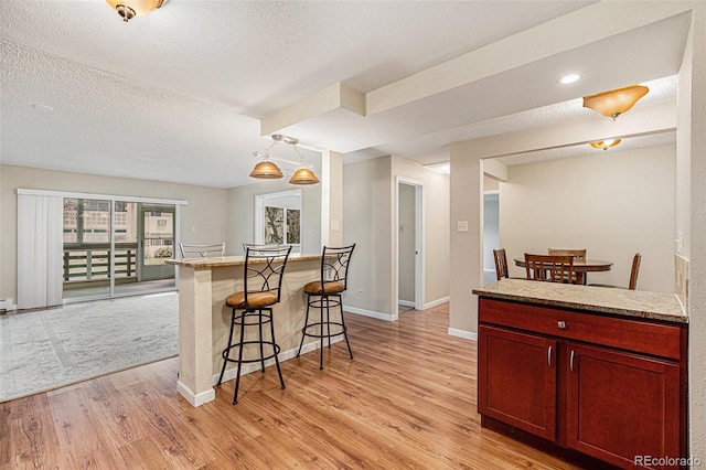 kitchen with a textured ceiling, a kitchen breakfast bar, hanging light fixtures, and light hardwood / wood-style flooring