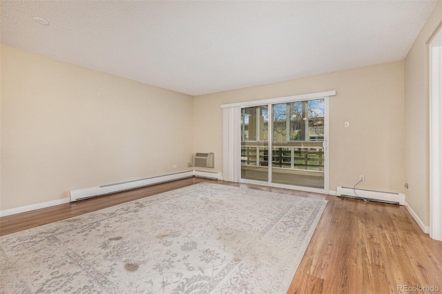 spare room with baseboard heating, a wall mounted AC, light hardwood / wood-style flooring, and a textured ceiling