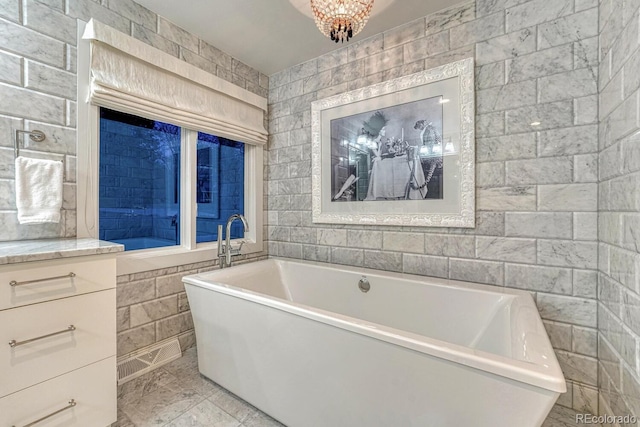 bathroom with marble finish floor, a freestanding bath, and tile walls