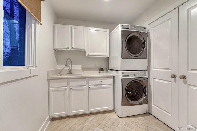 laundry area with stacked washer / dryer, a sink, cabinet space, and baseboards