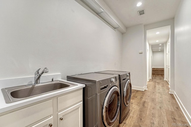 washroom with a sink, visible vents, baseboards, light wood-style floors, and washer and clothes dryer