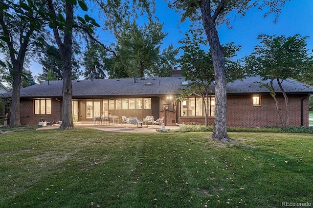 rear view of property with a patio area, a chimney, brick siding, and a yard