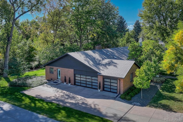 exterior space featuring concrete driveway, brick siding, a chimney, and an attached garage