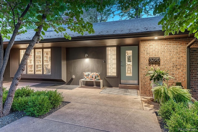 entrance to property featuring brick siding and a shingled roof