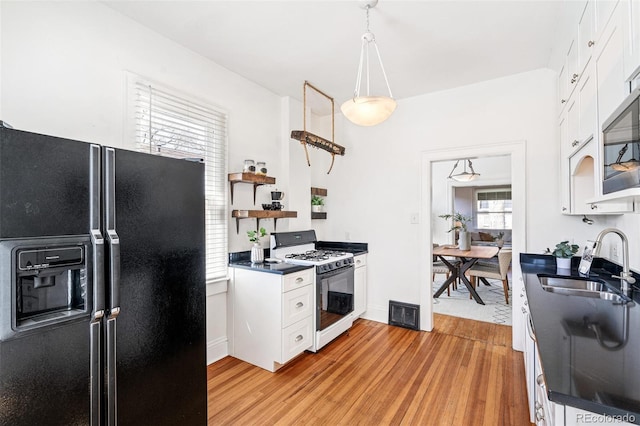 2826 Quitman St, Denver, CO 80212 - kitchen with black fridge, white gas range, dark countertops, light wood-style flooring, and white cabinetry