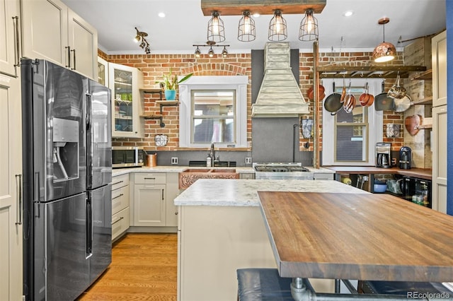 3811 N Clay St, Denver, CO 80211 - kitchen with ornamental molding, brick wall, light wood-style flooring, appliances with stainless steel finishes, and wall chimney exhaust hood