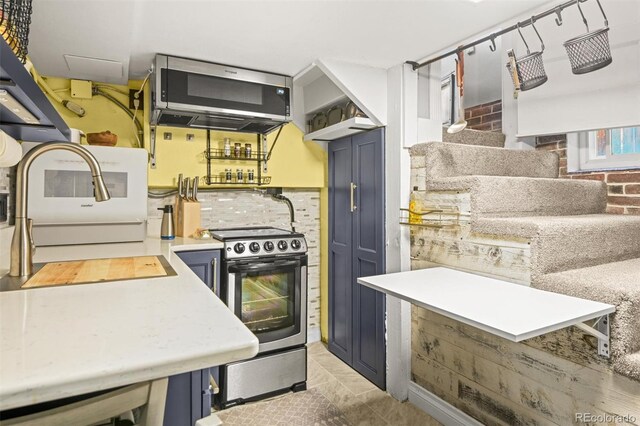 3811 N Clay St, Denver, CO 80211 - kitchen with blue cabinetry, light countertops, tasteful backsplash, stainless steel electric range oven, and brick wall