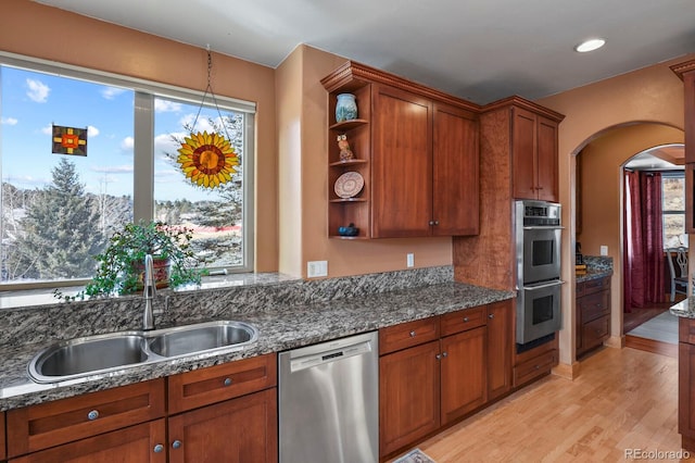 kitchen with sink, light wood-type flooring, stainless steel appliances, and dark stone counters