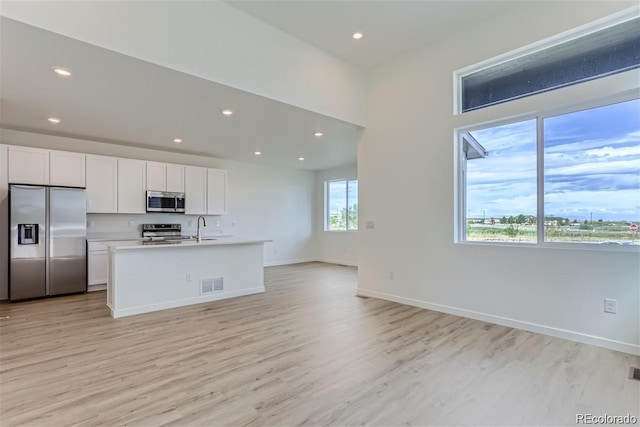 kitchen featuring white cabinetry, sink, stainless steel appliances, an island with sink, and light hardwood / wood-style floors