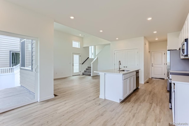 kitchen featuring stainless steel appliances, a kitchen island with sink, sink, white cabinets, and light hardwood / wood-style floors